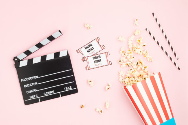 Movie clapperboard, tickets and popcorn over pink background. Movie night, home cinema, party invitation